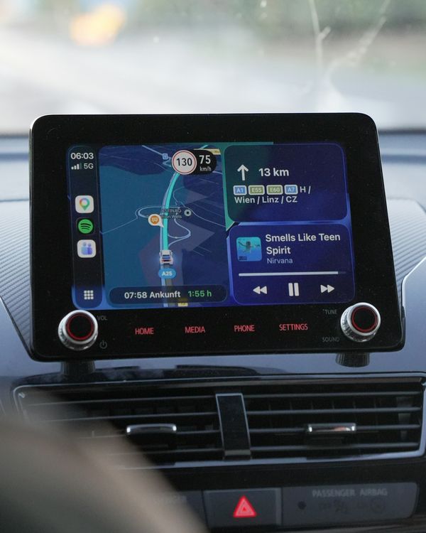 A touchscreen car stereo showing navigation and music, mounted in a car dashboard